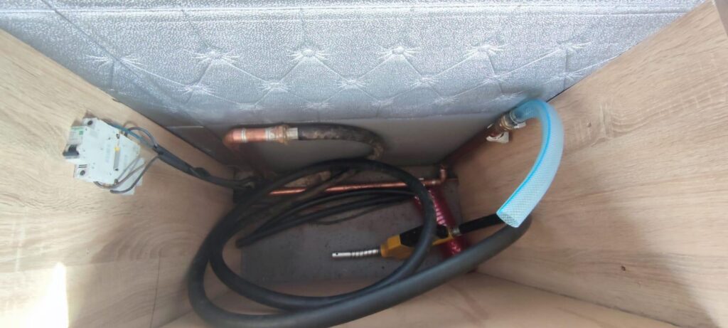 Under-sink area with tangled electrical cables, copper water pipes, and a blue supply hose connected to a valve.