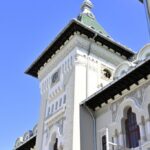 White clock tower with a green roof and decorative trim against a clear blue sky.