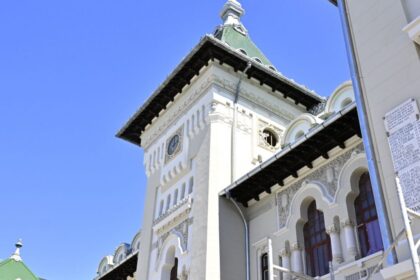 White clock tower with a green roof and decorative trim against a clear blue sky.
