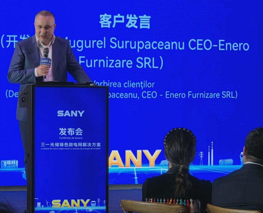 Man in a suit giving a speech at a blue SANY conference podium with a microphone in hand, backdrop shows Chinese and English text.