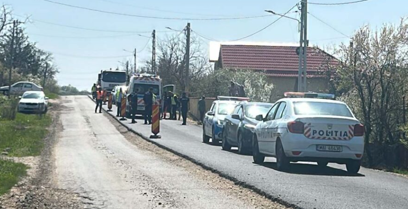 Police and road workers conducting a roadside stop on a rural street, with a police car, a worker in a reflective vest, and traffic cones along the road.