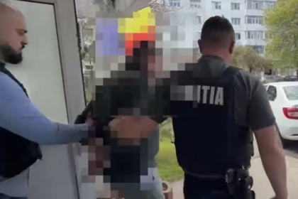 Police officer in a dark uniform with 'POLITIA' on the back restrains a person near a doorway outside, in a pixelated scene for privacy.