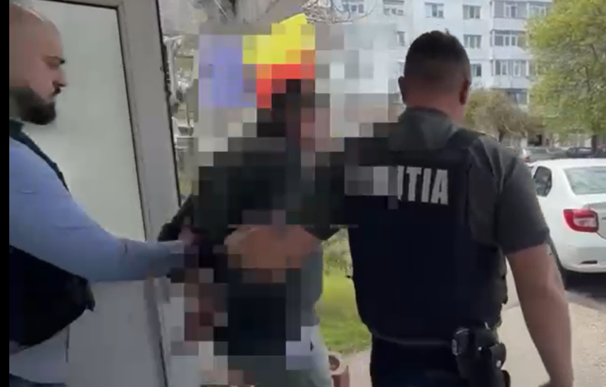 Police officer in a dark uniform with 'POLITIA' on the back restrains a person near a doorway outside, in a pixelated scene for privacy.