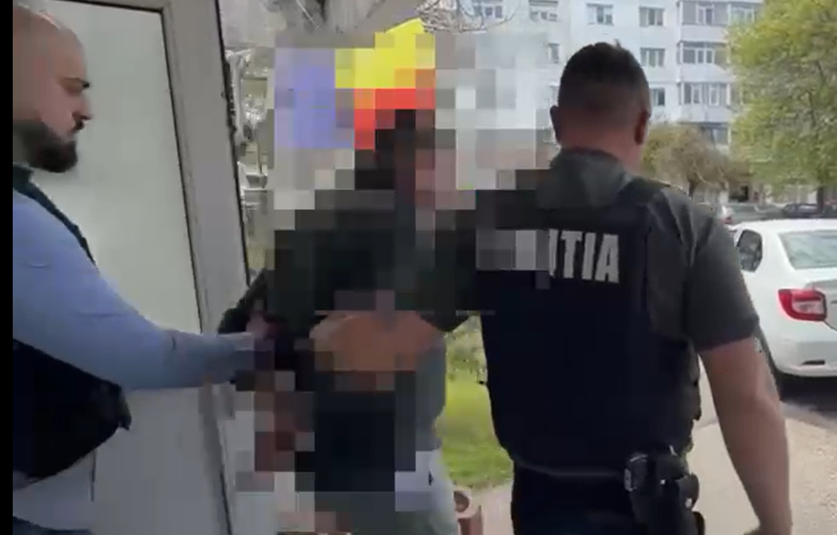 Police officer in a dark uniform with 'POLITIA' on the back restrains a person near a doorway outside, in a pixelated scene for privacy.