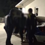 Nighttime scene of Romanian police officers in protective vests detaining a person beside a car outdoors; 'Politia Romana' watermark at top.