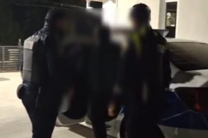 Nighttime scene of Romanian police officers in protective vests detaining a person beside a car outdoors; 'Politia Romana' watermark at top.