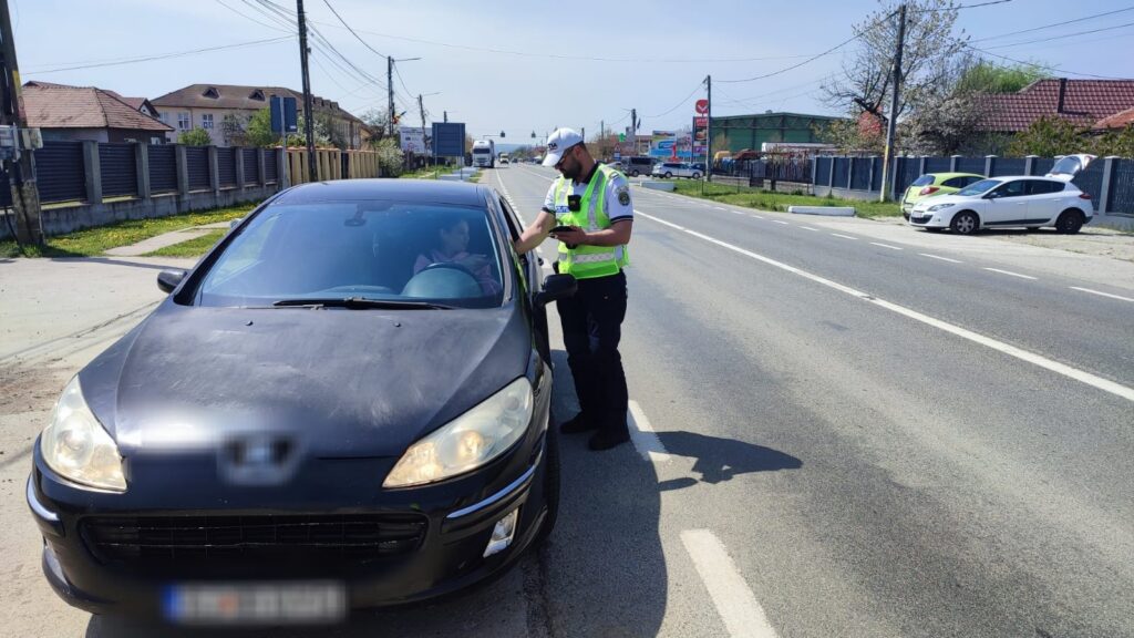 Traffic officer in a neon vest checks a driver in a dark blue sedan on a sunny suburban street.