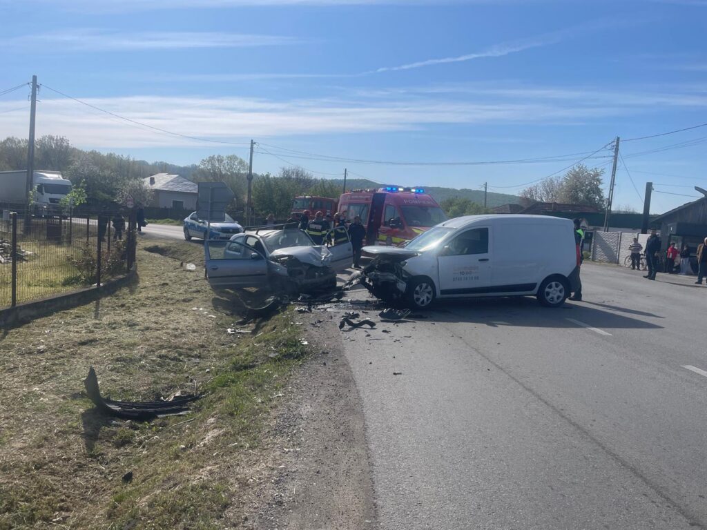 Two damaged cars in the middle of a rural road after a collision, with emergency responders and a red ambulance nearby
