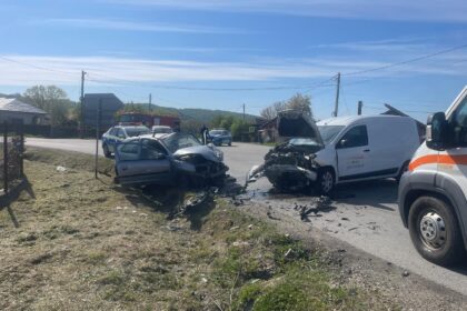 Two cars severely damaged in a head-on collision on a rural road, with debris and trucks nearby and emergency responders on the scene.