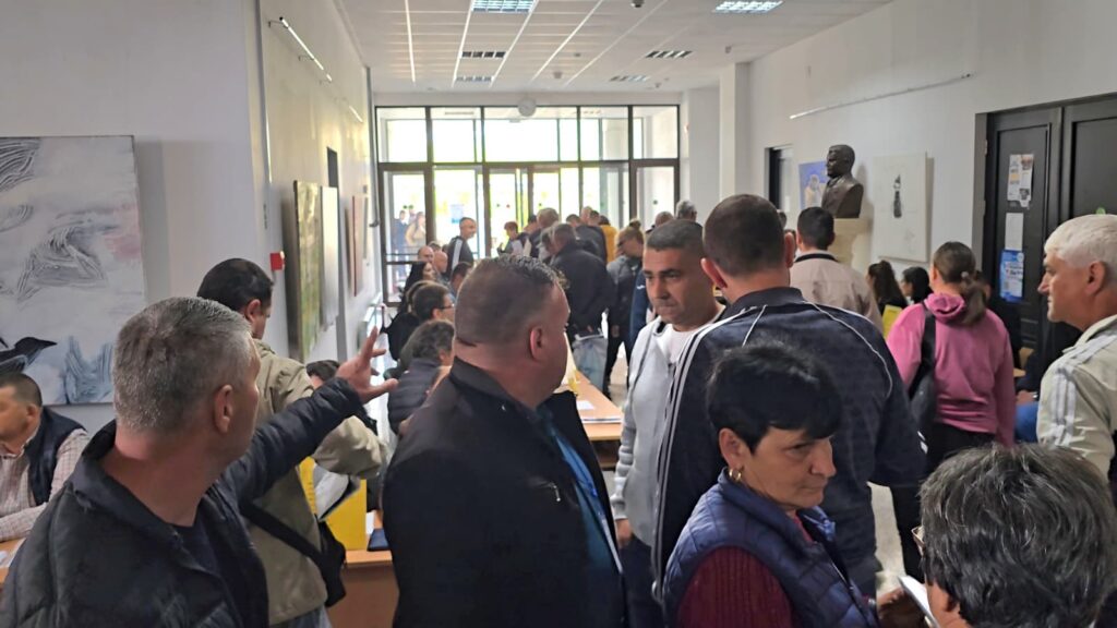 Crowded lobby with people queuing at desks along the left, glass doors at the far end.