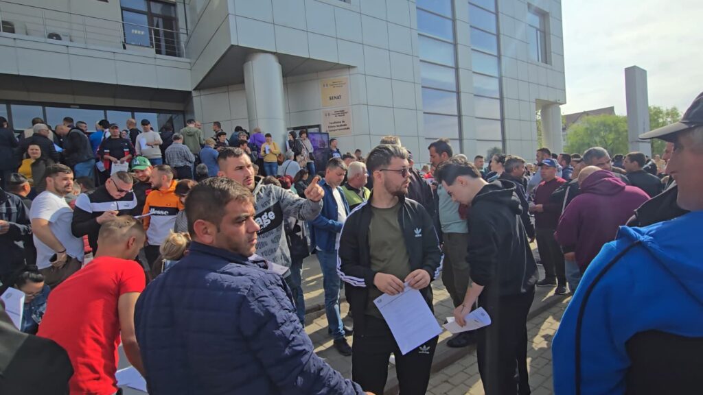 Crowd of people gathered outside a modern office building, many holding papers and conversing.