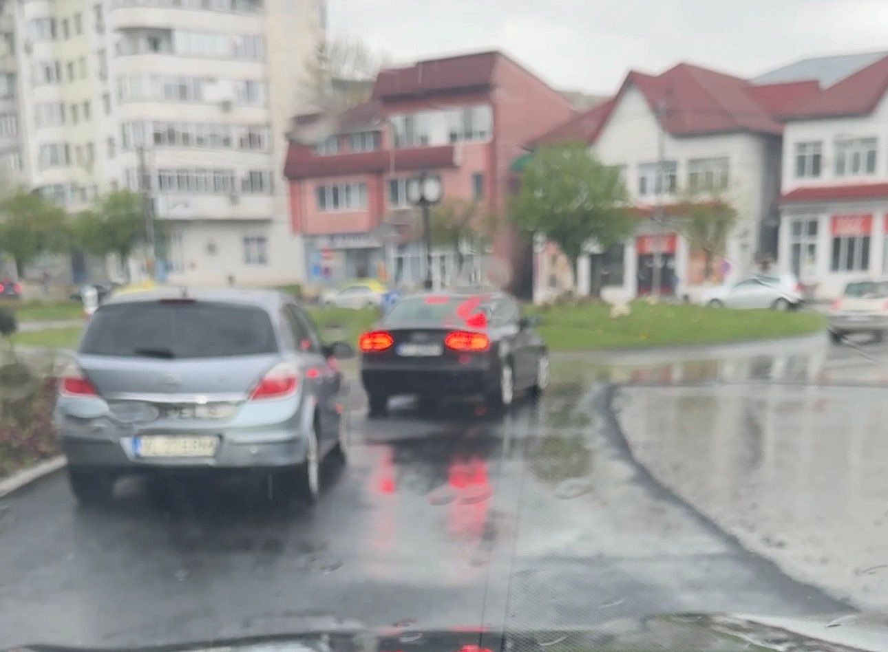 Blurred urban street after rain: cars drive on a wet, reflective road with puddles and blurred buildings in the background.