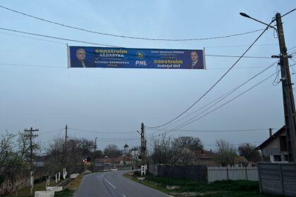 Blue political campaign banner stretched between utility poles over a residential road, showing two men in suits and campaign text (PNL) and the word 'construi m' visible.