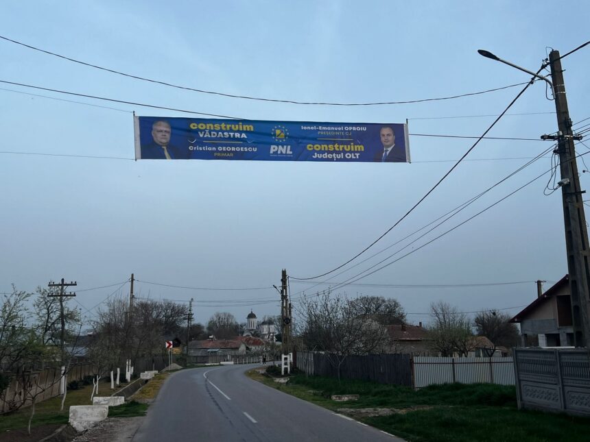 Blue political campaign banner stretched between utility poles over a residential road, showing two men in suits and campaign text (PNL) and the word 'construi m' visible.