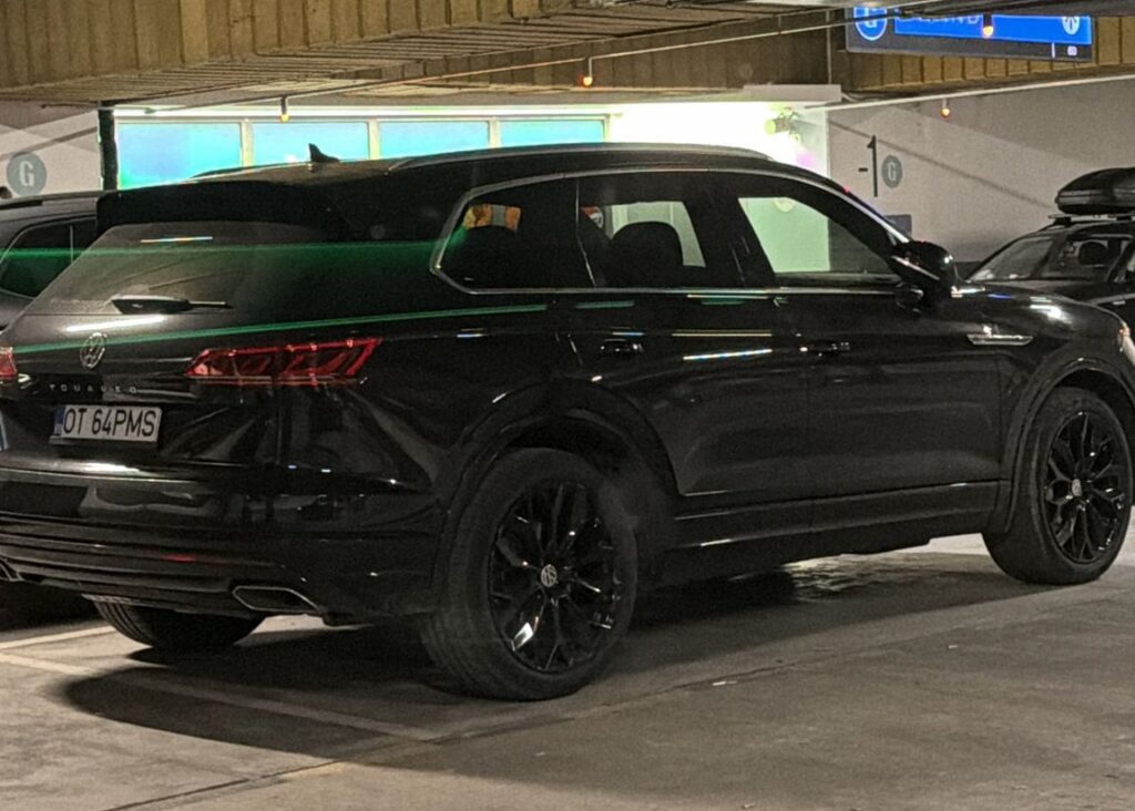 Black Volkswagen Touareg SUV parked in a dim, multi‑level garage with dark alloy wheels and a roof rack/box, tinted windows.
