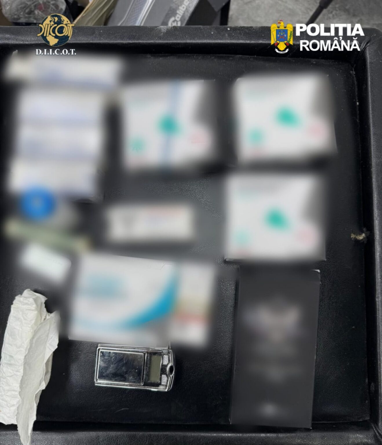 Open black case with several blurred boxes and a small lighter; logos for D.I.C.O.T. and Politia Română visible at top corners, suggesting seized evidence.