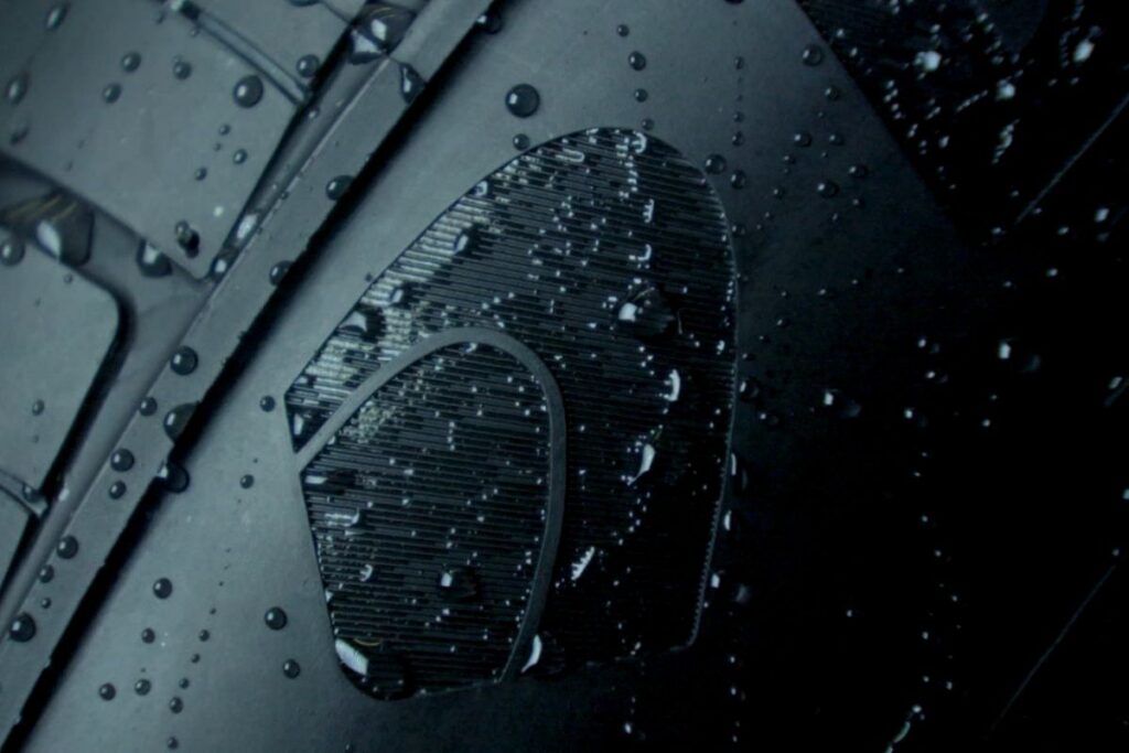 Close-up of a metallic circular vent or grill with water droplets on a dark panel, showing riveted metal and a curved edge.