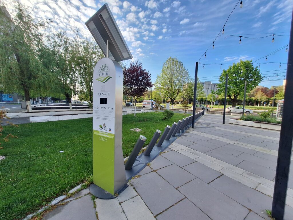 Tall metal information pillar in a park with a solar panel on top and a bike icon on the sign.