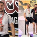Male athlete posing with a red medal in a white shirt, standing in front of an event banner indoors.