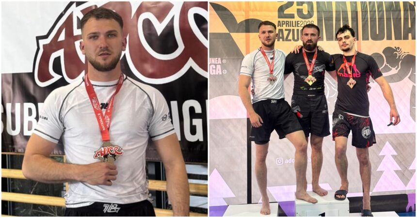 Male athlete posing with a red medal in a white shirt, standing in front of an event banner indoors.