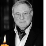 Portrait of an elderly man in a suit with glasses, a scarf, and a lit candle in the foreground (black and white).