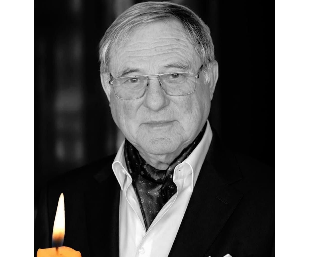 Portrait of an elderly man in a suit with glasses, a scarf, and a lit candle in the foreground (black and white).