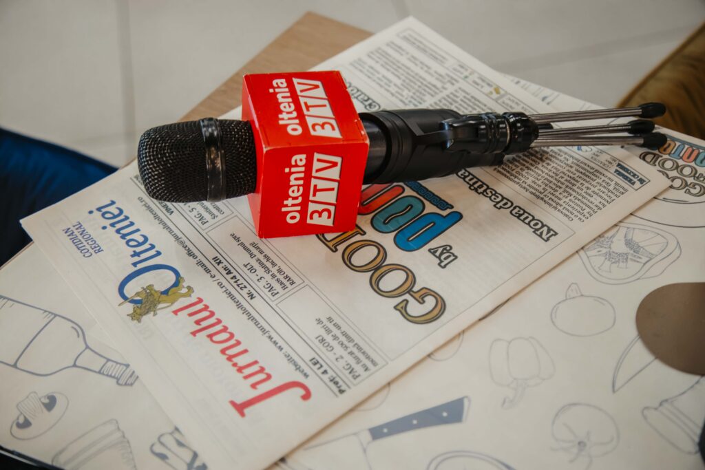 Red broadcast microphone resting on a newspaper, suggesting a press interview setup.