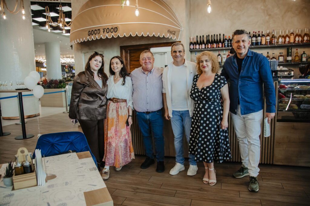 Six adults posing together in a casual restaurant bar area, with bottles on the back shelves and warm lighting behind them.