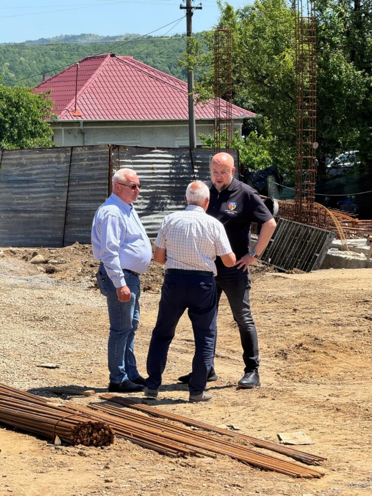 - Jurnalul Olteniei – Știri din Craiova și Oltenia Three men stand in a casual discussion at a construction site, with steel rebar and dirt ground in the foreground and a house with a red roof in the background.