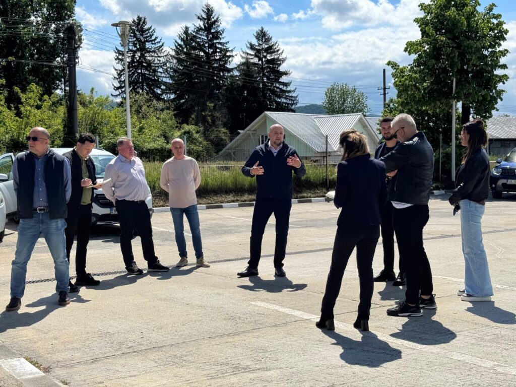 Group of eight people standing in a parking lot, listening to a man gesturing as he speaks outdoors.
