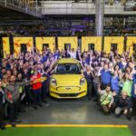 Factory workers celebrate around a yellow Ford Puma, holding a 'PUMA ONE MILLION' sign in an automotive plant.