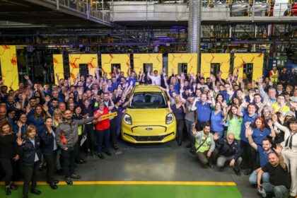 Factory workers celebrate around a yellow Ford Puma, holding a 'PUMA ONE MILLION' sign in an automotive plant.