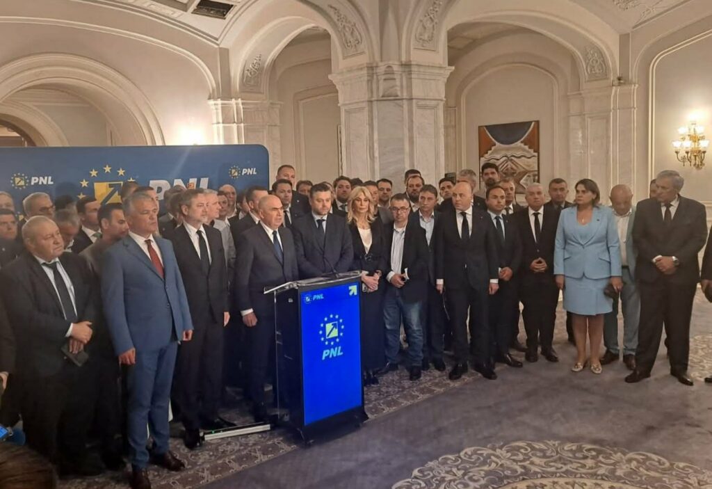 Group of suited politicians and staff pose at a press event around a blue podium with the PNL logo in a grand room.