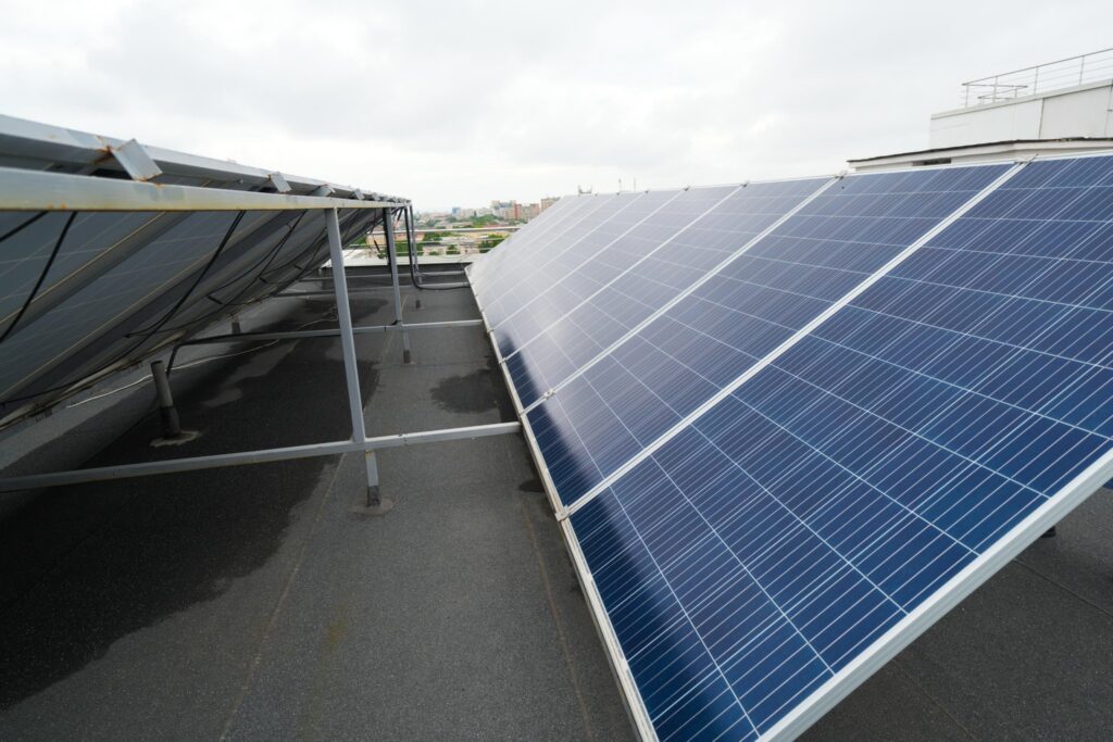 Rooftop solar panels angled for sunlight with an urban skyline in the distance under a cloudy sky.