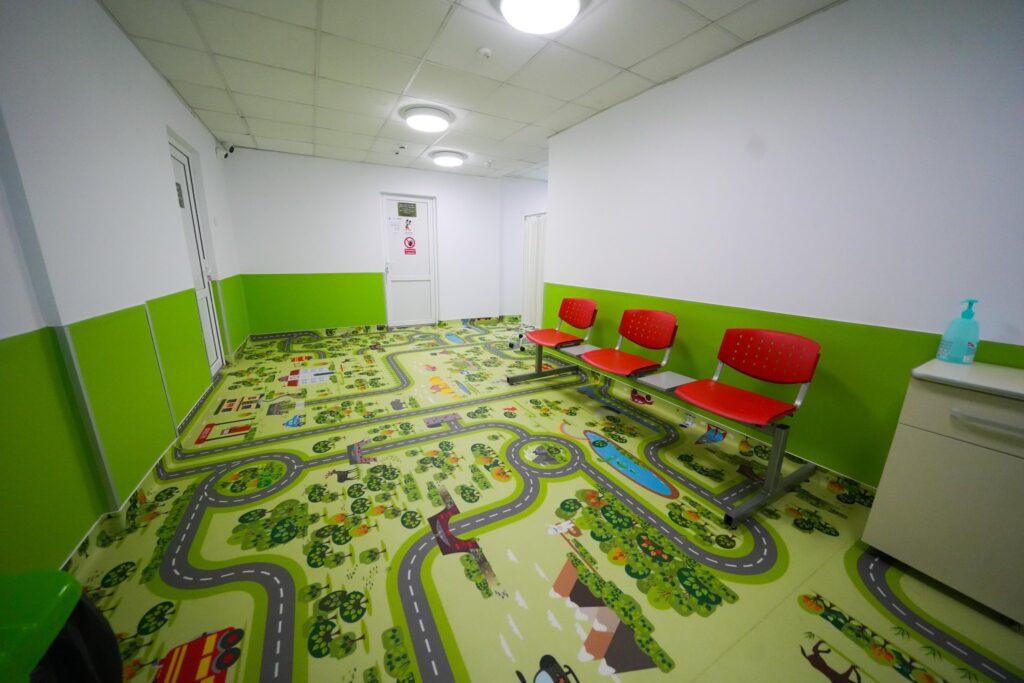 Playroom for kids with a road-themed floor, green lower walls, white upper walls, and red chairs along the right side.