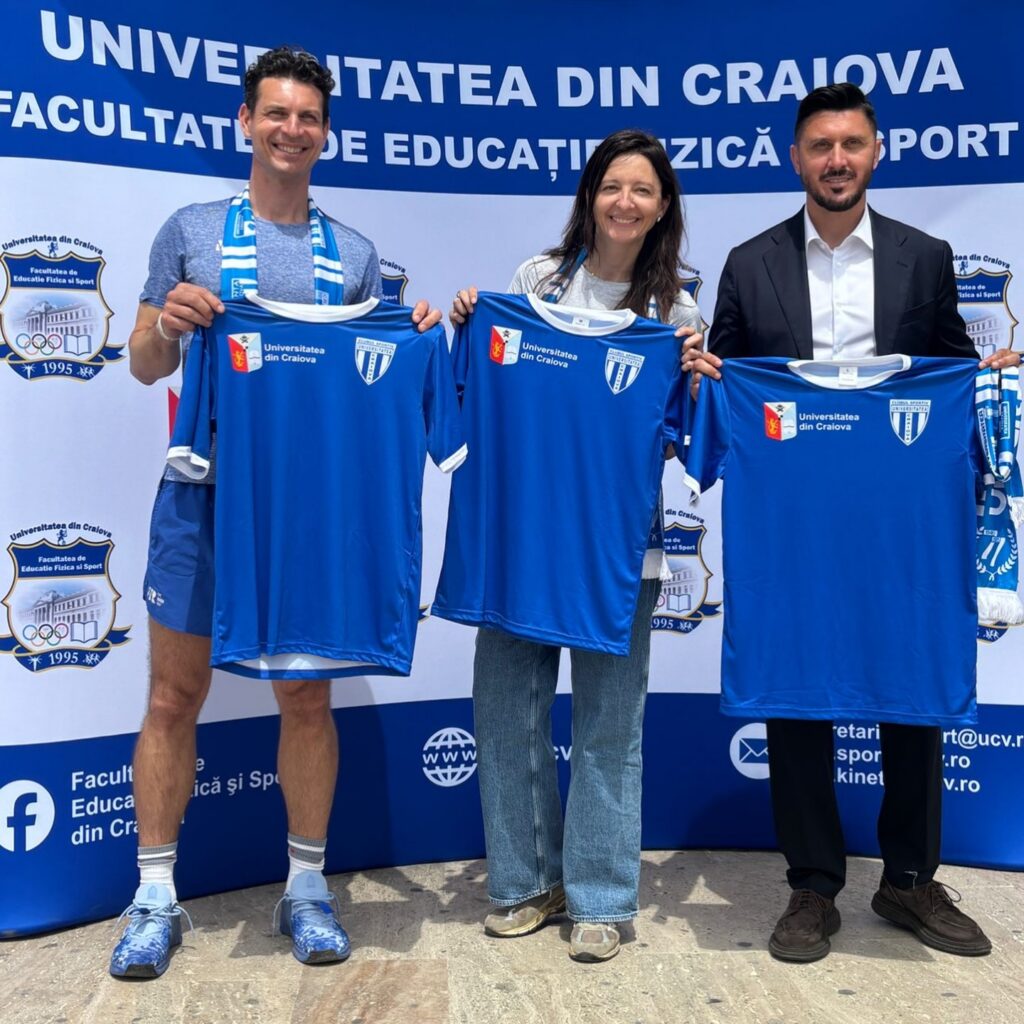 Three people stand in front of a university banner, each holding a blue jersey with the Craiova University logos visible on the shirts.