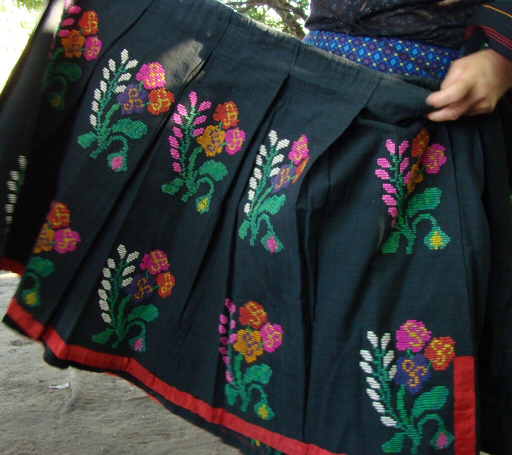 Navy skirt with bright, multicolored floral embroidery and a red hem, held by a hand at the waist.
