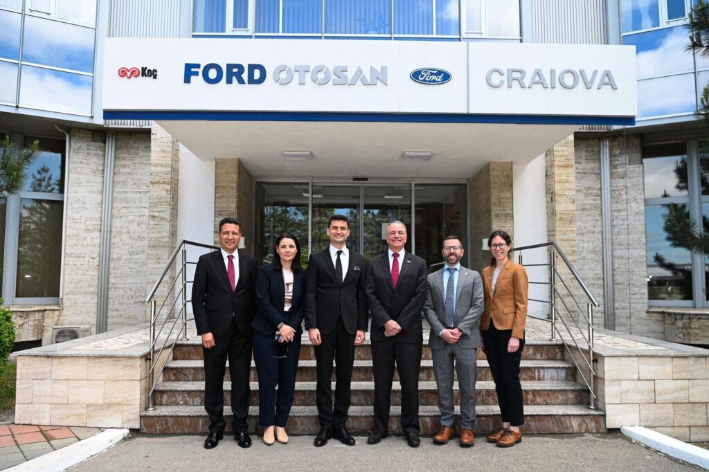 Six professionals in business attire pose on the steps of a modern office building with Ford Craiova signage above the entrance.