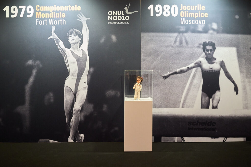 - Jurnalul Olteniei – Știri din Craiova și Oltenia Museum display with split black-and-white sports photos (1979 Fort Worth and 1980 Moscow) and a small doll in a glass case at center.
