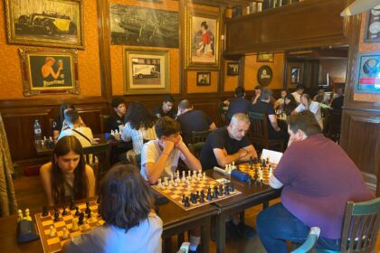 Group of people playing chess in a cozy vintage-style cafe with wood-paneled walls and framed art behind them