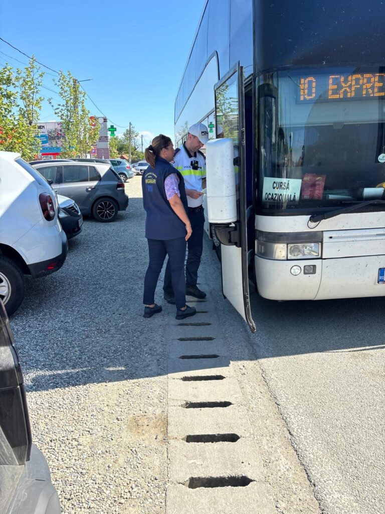 Two uniformed staff members speak beside a large bus with its door open in a parking lot.