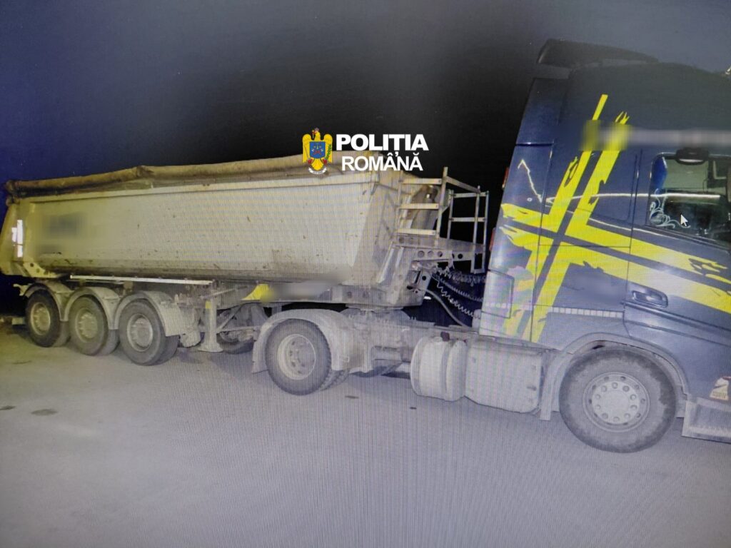 Nighttime accident scene with a blue and yellow police truck beside a large silver trailer against a dark sky; Romanian Police watermark centered.
