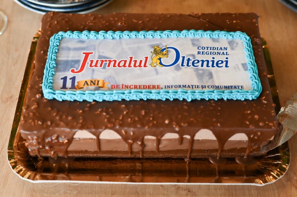 Chocolate cake with a blue piped border and an edible sheet reading 'Jurnalul Olteniei' and '11 ANI' for an 11-year celebration.