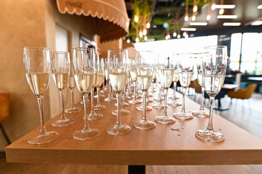 Row of champagne flutes on a wooden table in a bright, modern event space.