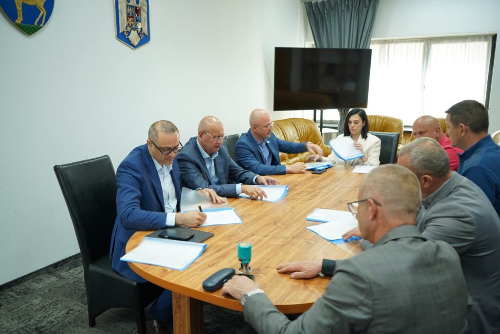 WhatsApp Image 2026-05-19 at 112735 1 - Jurnalul Olteniei – Știri din Craiova și Oltenia Several professionals sit around a wooden conference table reviewing documents in a formal meeting room.