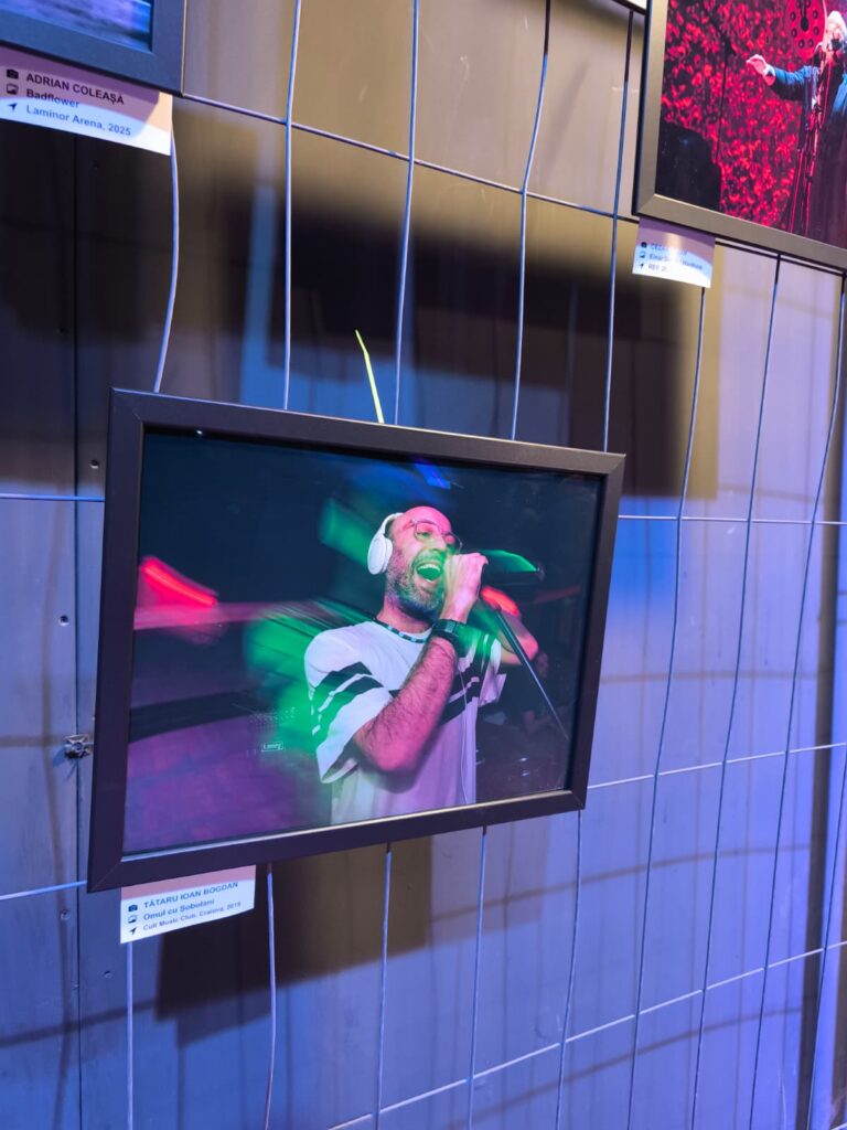 Framed photo of a man singing into a microphone while wearing white headphones, displayed on a blue tiled wall with neon lighting.