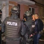 Nighttime scene of Romanian police in tactical gear surrounding and restraining a man outside a residential building.