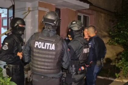 Nighttime scene of Romanian police in tactical gear surrounding and restraining a man outside a residential building.