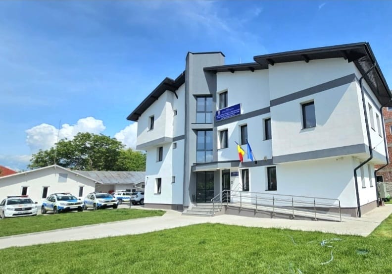 Modern white two-story building with blue accents, flagpoles, and a ramp on a sunny day.