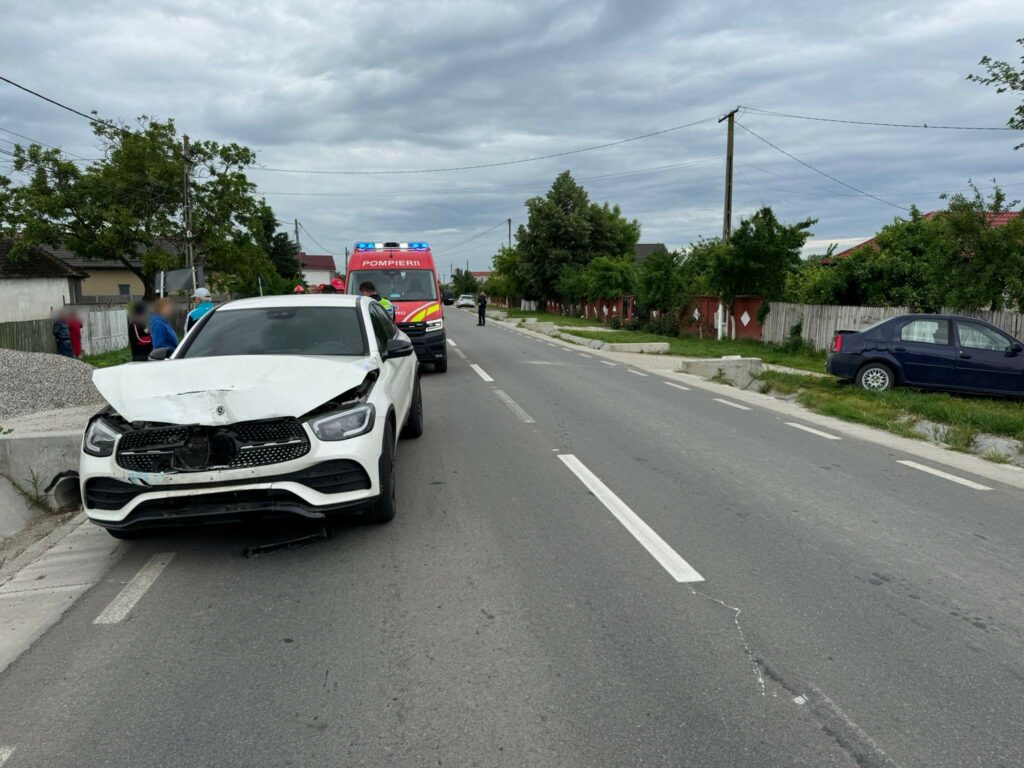 White SUV with significant front-end damage parked on a residential street, emergency vehicle with blue lights in the background.